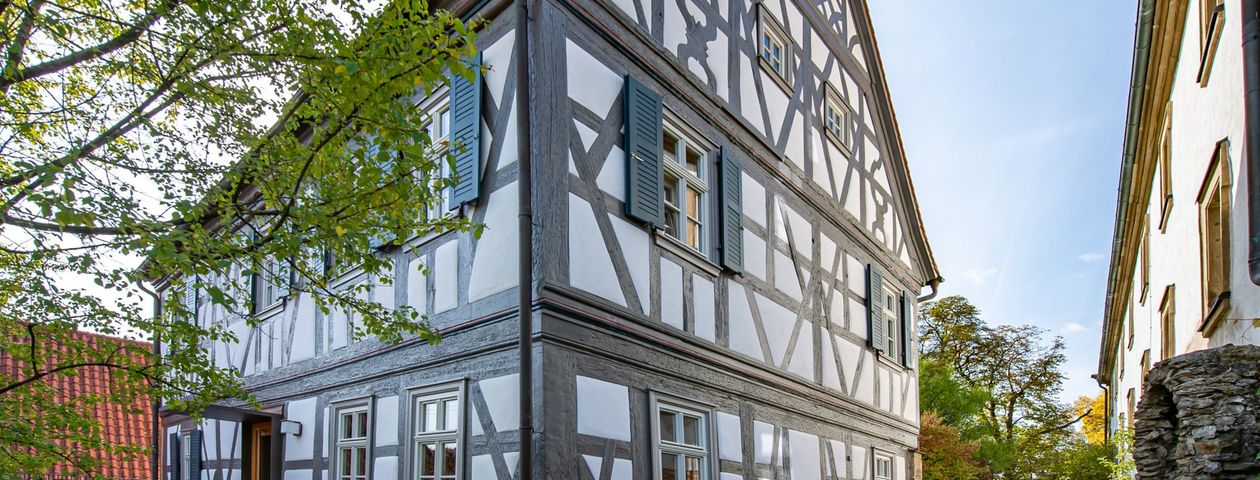 Saniertes Fachwerkhaus vor blauem Himmel neben einem grünen Baum