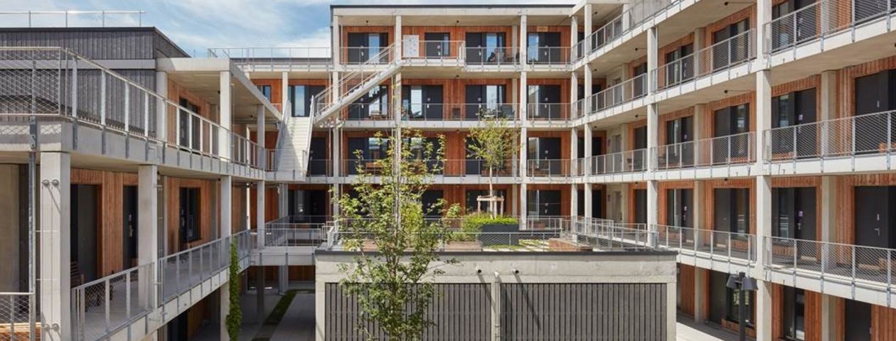 Mehrgeschossige Holz-Stahl-Häuser mit Laubengängen um einen grünen Innenhof